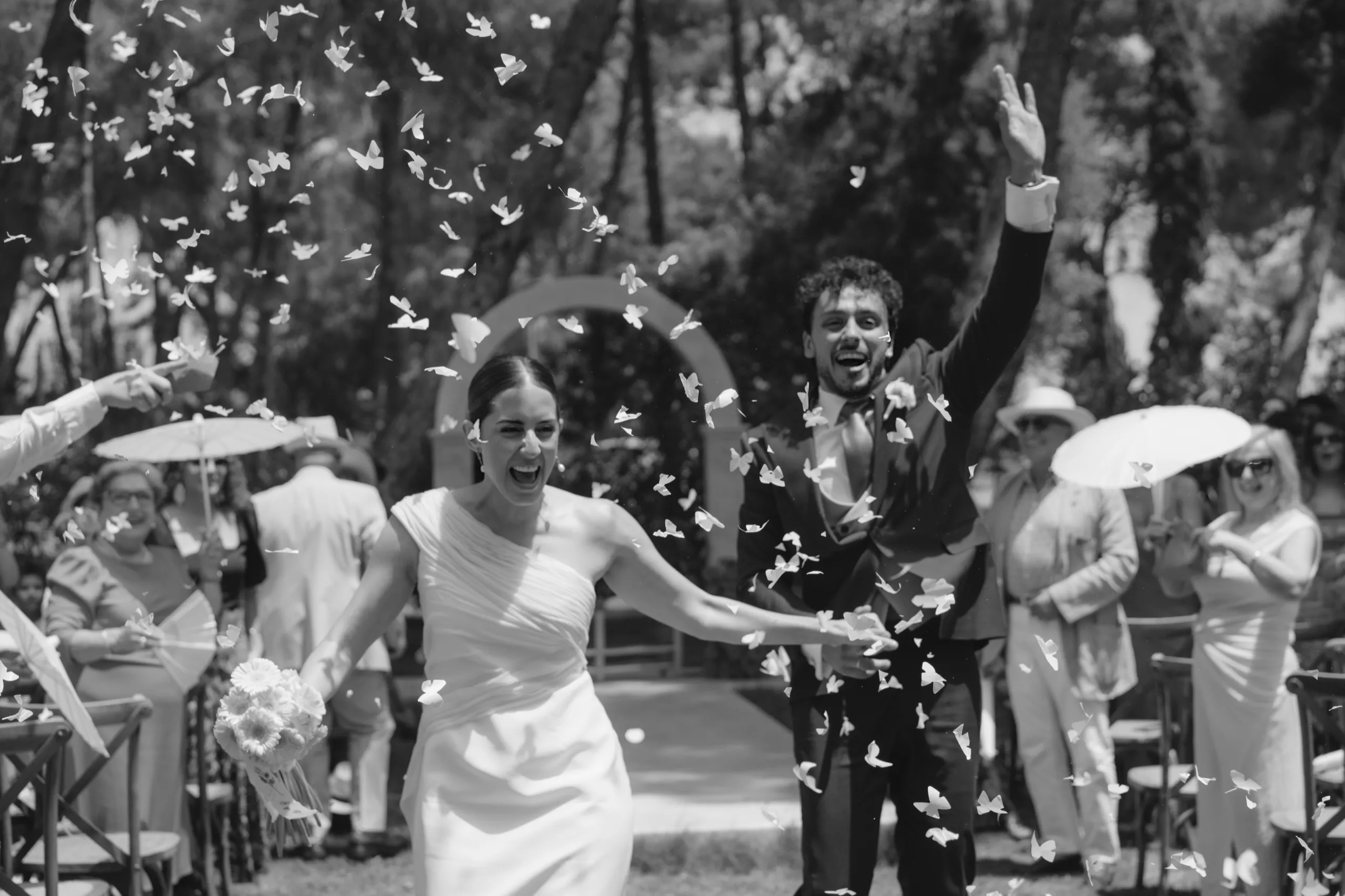 Novios saliendo de la ceremonia entre una lluvia de mariposas de papel, en blanco y negro