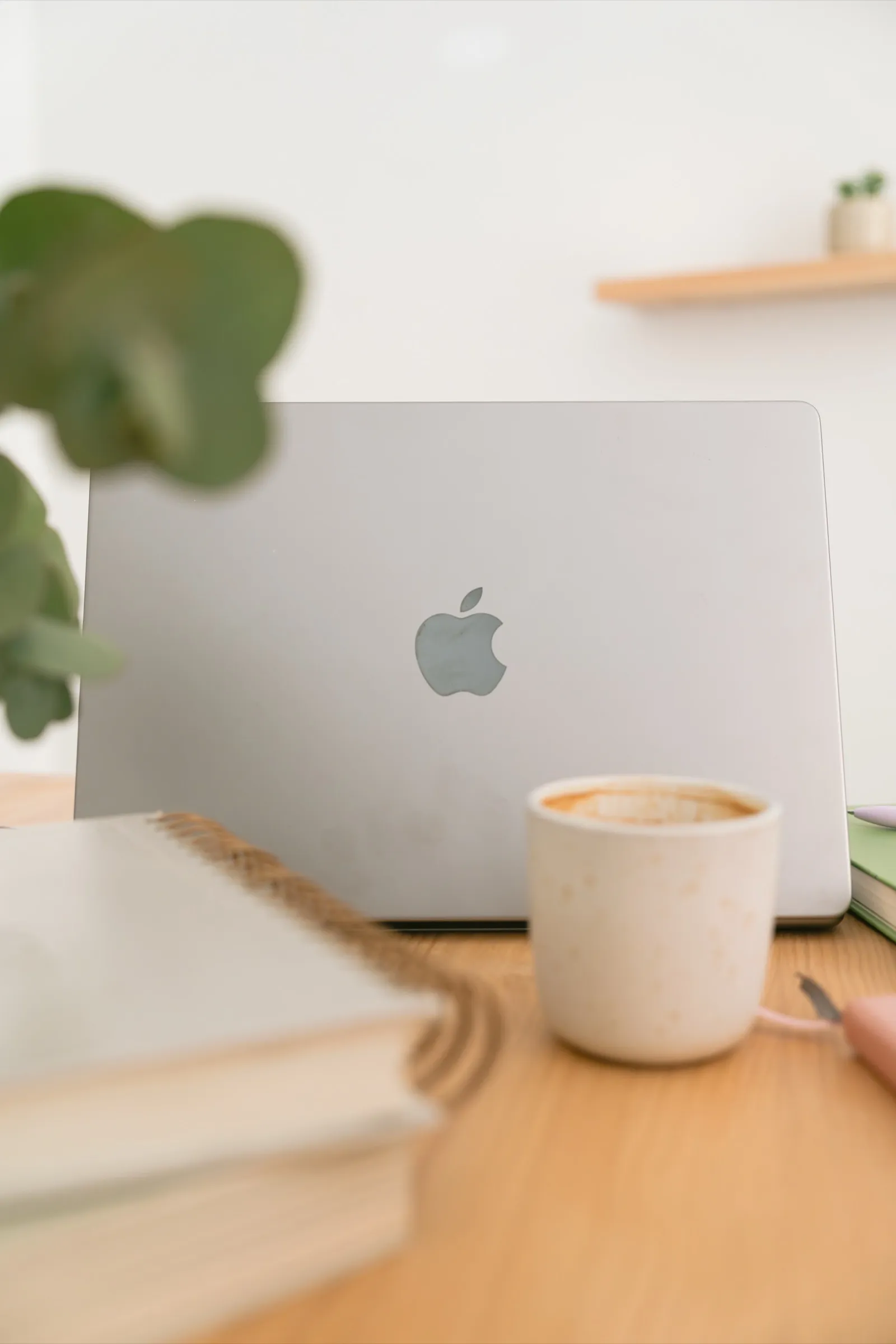 Portátil sobre una mesa de madera junto a una taza de café, una libreta y una planta