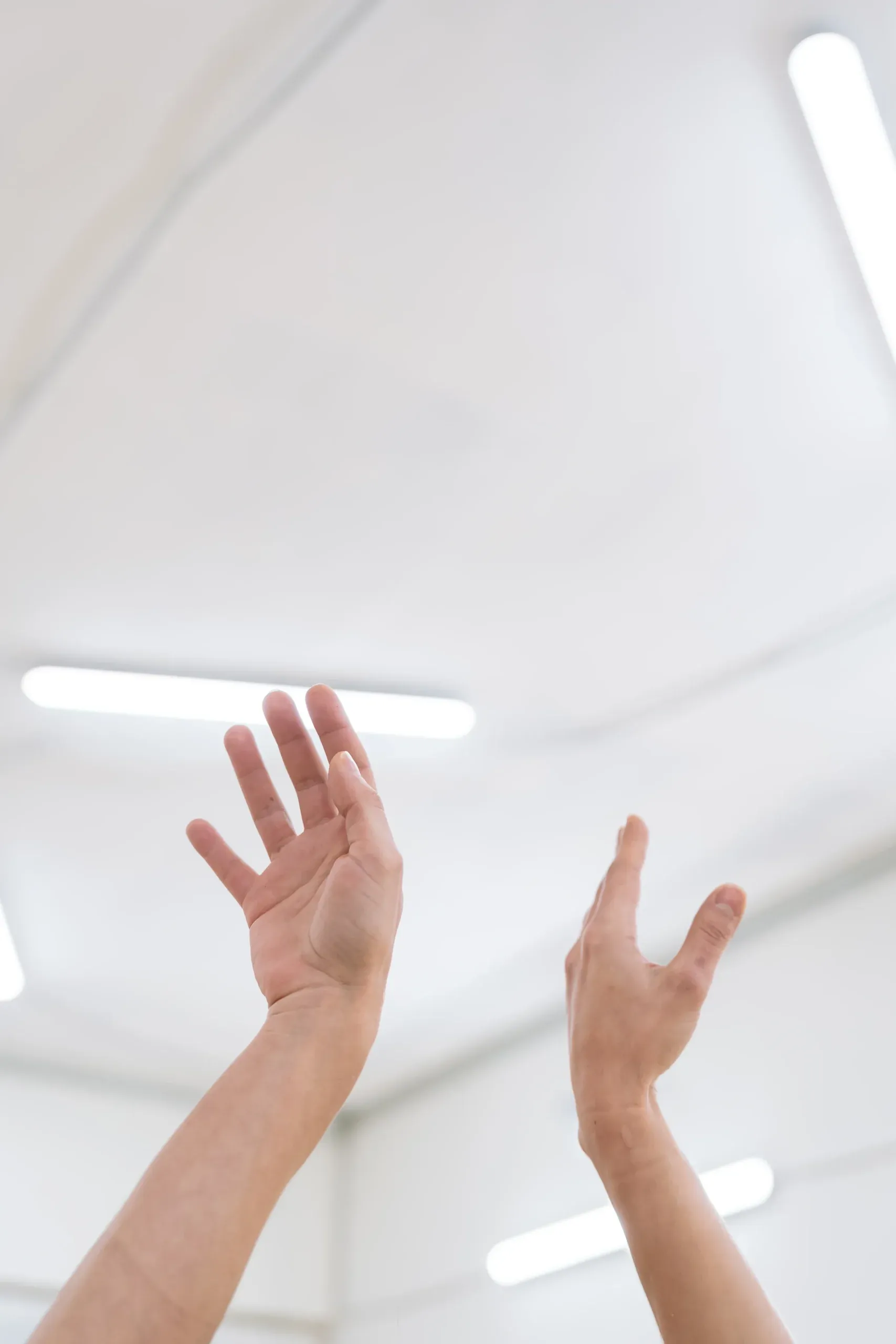 Manos alzadas hacia un techo blanco iluminado